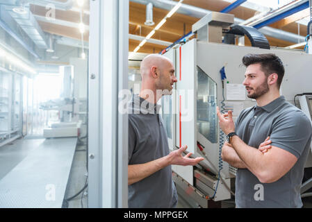 Two men discussing at machine in modern factory Stock Photo
