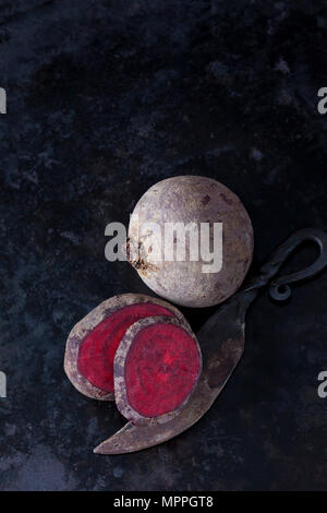 Whole and sliced beetroot and an old knife on dark metal Stock Photo