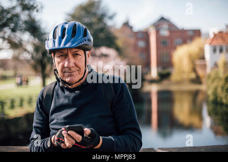 Portrait of senior man with cycling helmet using smartphone Stock Photo