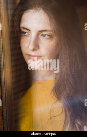 Portrait of pensive young woman with long brown hair looking out of window Stock Photo