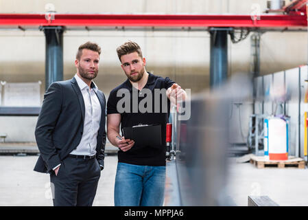 Two men with clipboard talking on factory shop floor