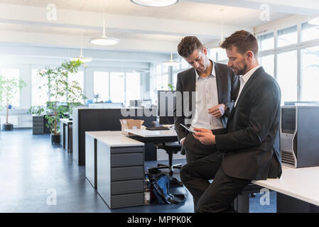 Two businessmen standing in office, discussing solutions, using digital tablet Stock Photo