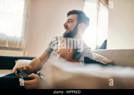 Father and son sitting together on the couch playing computer game Stock Photo