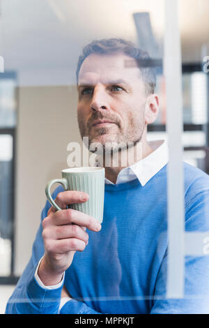 Focused businessman holding cup of coffee looking at glass pane Stock Photo