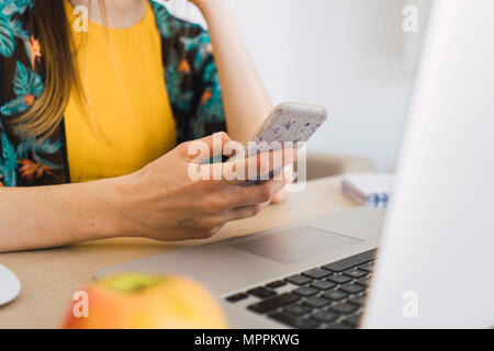Close-up of woman sitting at table at home using cell phone and laptop