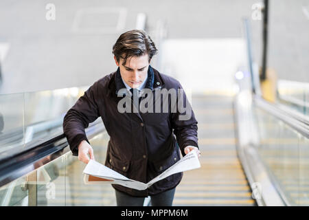 Businessman on escalator reading a newspaper Stock Photo