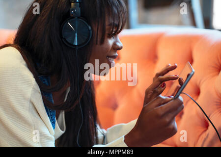 Smiling young woman on the couch using tablet and headphones Stock Photo