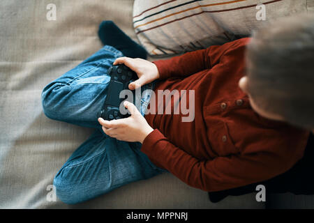 Little boy sitting on the couch playing computer game, top view Stock Photo