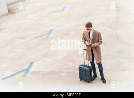 Businessman with rolling suitcase using smartphone at parking garage Stock Photo