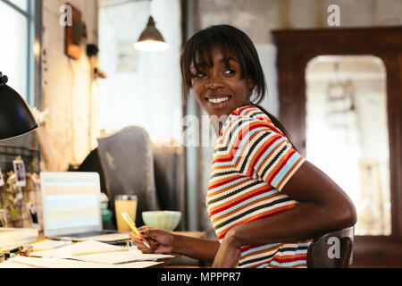 Portrait of smiling young woman sitting at desk in a loft Stock Photo