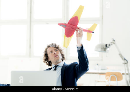 Businessman sitting in his office playing with a toy plane Stock Photo