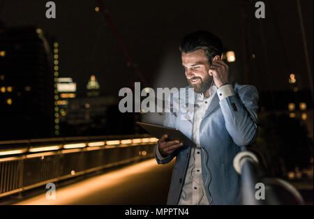 Young man on bridge at night with world map emerging from tablet Stock Photo