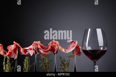 Prosciutto with thyme twigs and glass of red wine on a dark background. Copy space for your text. Stock Photo