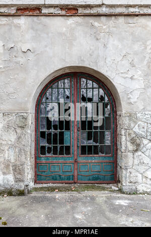 Vintage door with broken windows on the facade of an old building stone wall. Stock Photo