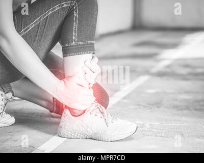 Black and white young woman suffering from an ankle injury while exercising and running. Sport  excercise concept. Stock Photo