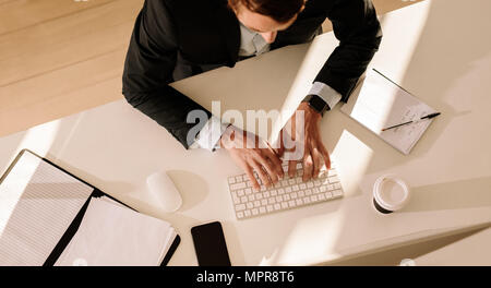 Top view of a businessman entering text in computer using keyboard with documents and a coffee glass on the table. Man using wireless keyboard and mou Stock Photo