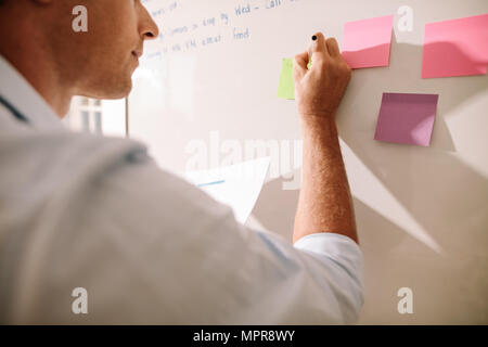 Entrepreneur making notes on the colorful sticky notes placed on the board. Stock Photo