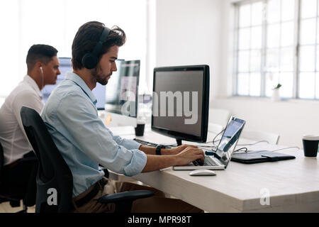 Software developers sitting at office working on computers wearing headphones. Application developer working on a laptop in office. Stock Photo