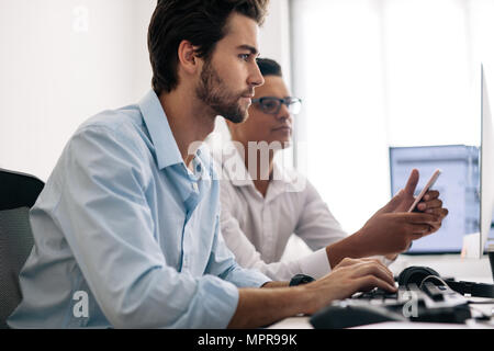 Application developers testing application on mobile phone in  office. Software developers sitting at office working on computers. Stock Photo