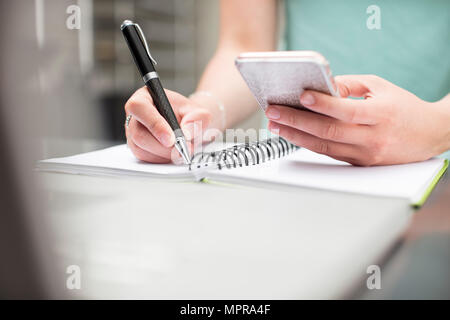 Woman writing notes in diary, holding smartphone Stock Photo