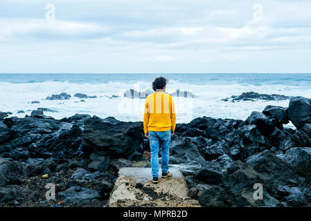 Azores, Sao Miguel, rear view of man looking at the sea from stony coast Stock Photo