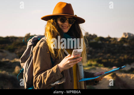 Italy, Sardinia, smiling woman on a hiking trip holding cell phone and map Stock Photo