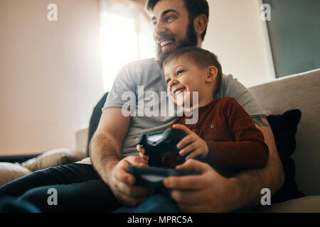 Happy father and little son sitting together on the couch playing computer game Stock Photo