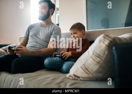 Father and son sitting together on the couch playing computer game Stock Photo