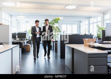 Two businessmen walking in office, using digital tablet, talking Stock Photo