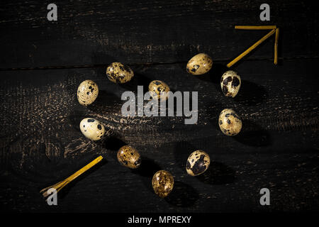 Quail eggs shaped as a heart and  arrow made of straw on dark wood Stock Photo