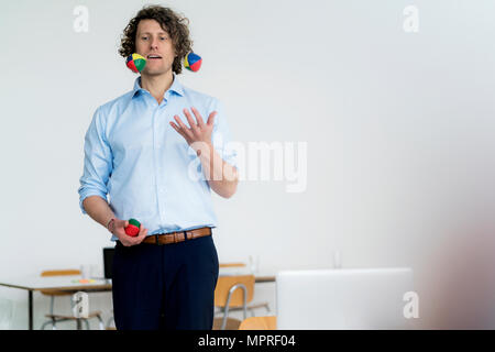 Smiling businessman juggling balls in his office Stock Photo