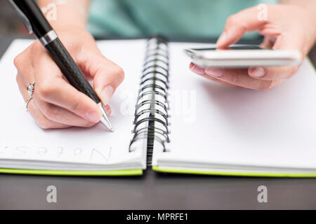 Woman writing notes in diary, holding smartphone Stock Photo