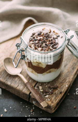 Coconut yoghurt and chocolate chia seed dessert with banana, topped with cacao nibs and hazelnuts Stock Photo