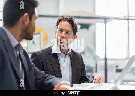Two businessmen sharing laptop in factory Stock Photo