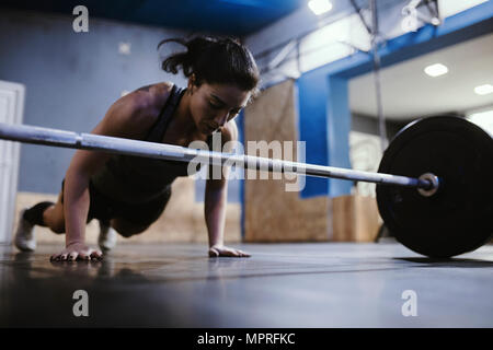 Woman doing push ups at barbell in gym Stock Photo