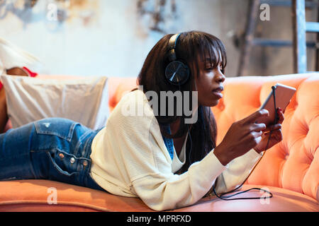 Young woman lying on the couch using tablet and headphones Stock Photo