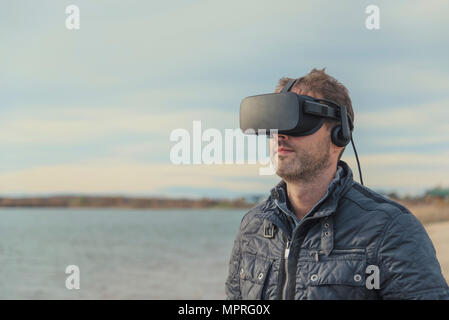 Man wearing VR glasses at lakeshore Stock Photo