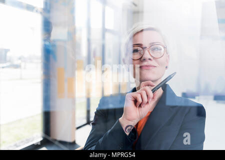 Portrait of confident businesswoman behind glass pane in office Stock Photo