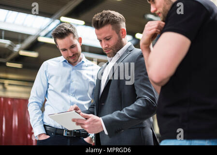 Three men sharing tablet on factory shop floor Stock Photo