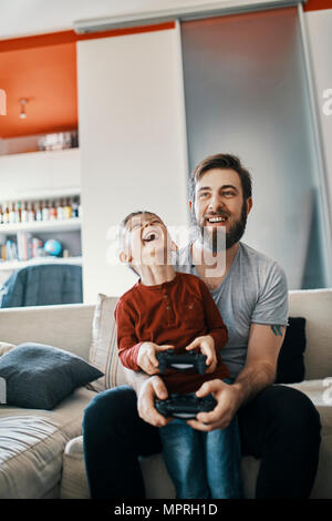 Father and son sitting together on the couch playing computer game Stock Photo