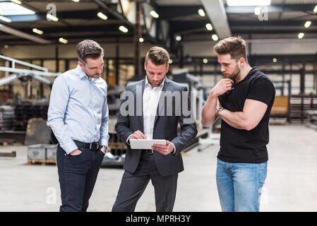 Three men sharing tablet on factory shop floor Stock Photo