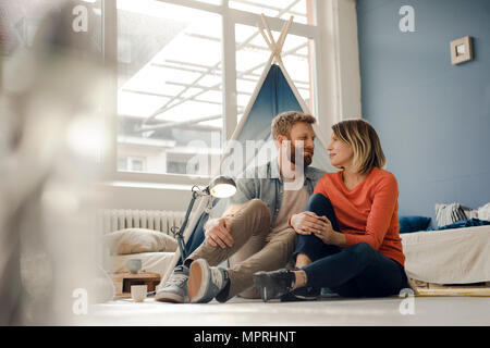 Affectionate couple sitting on ground, smiling happily Stock Photo