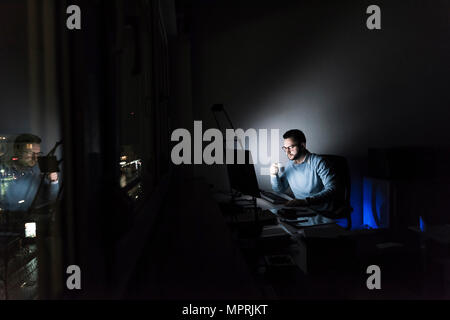 Businessman with cup of coffee working on computer in office at night Stock Photo