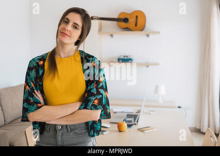 Portrait of smiling young woman at home with guitar on shelf Stock Photo