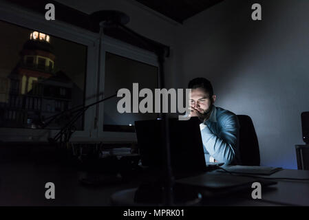 Businessman working on laptop in office at night Stock Photo