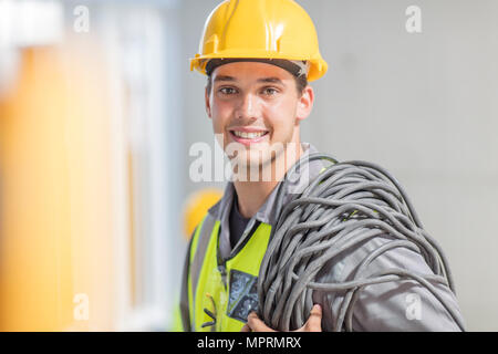 Portrait of smiling electrician with cable on construction site Stock Photo