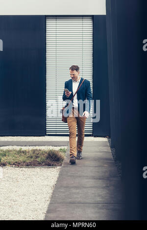 Businessman walking outdoors looking at smartphone Stock Photo
