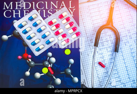 Pills on textbook of medicinal chemistry and stethoscope put on EKG or ECG (Electrocardiogram) graph report paper. Drug structure research concept. Ca Stock Photo