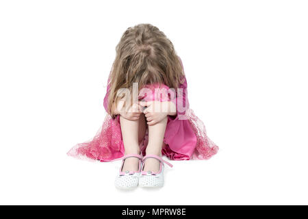 Portrait of a crying girl sitting on the floor, with a disheveled hairdress embracing her knees, isolated on a white background Stock Photo