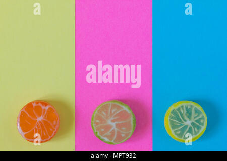 Creative view of colored candy in the form of citrus (orange, lime, lemon) in summer colors on a colored paper background. Conceptual image of summer. Stock Photo